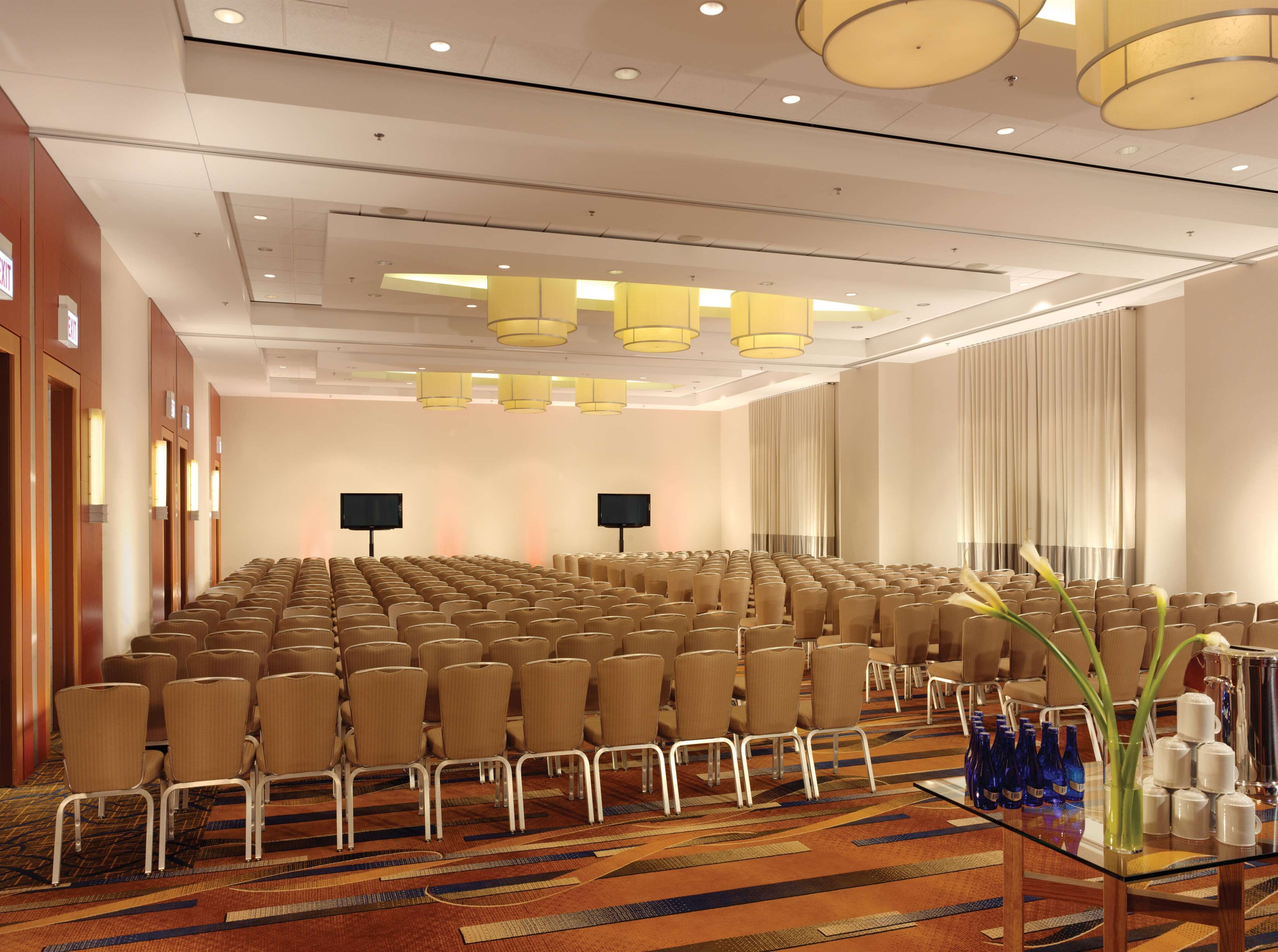 A conference room with rows of chairs, a glass table with water bottles, and a large window with curtains.
