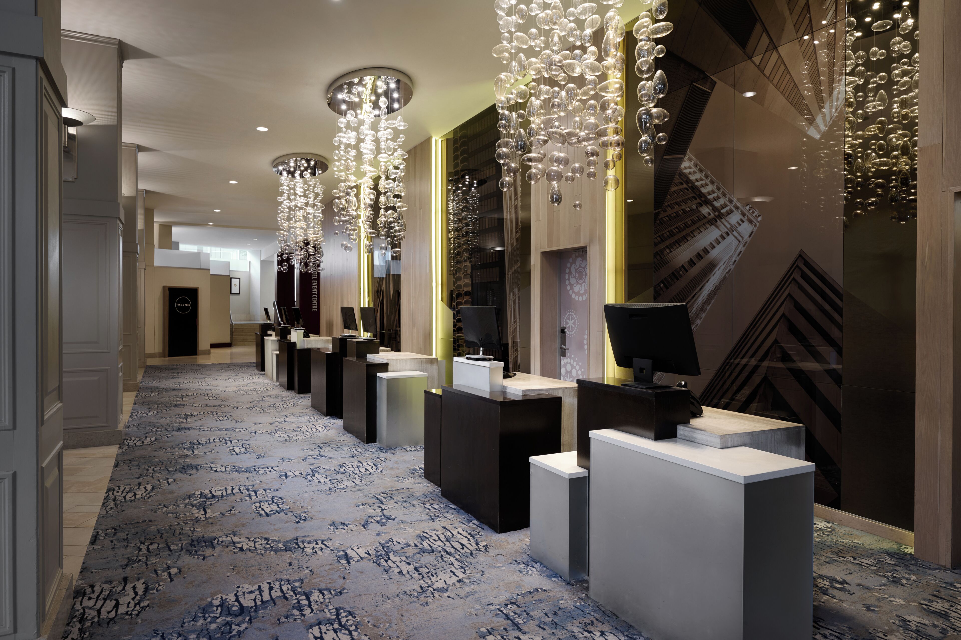 Un hall d’hôtel doté d’un long comptoir d’accueil, de lustres modernes et d’un tapis à motifs.