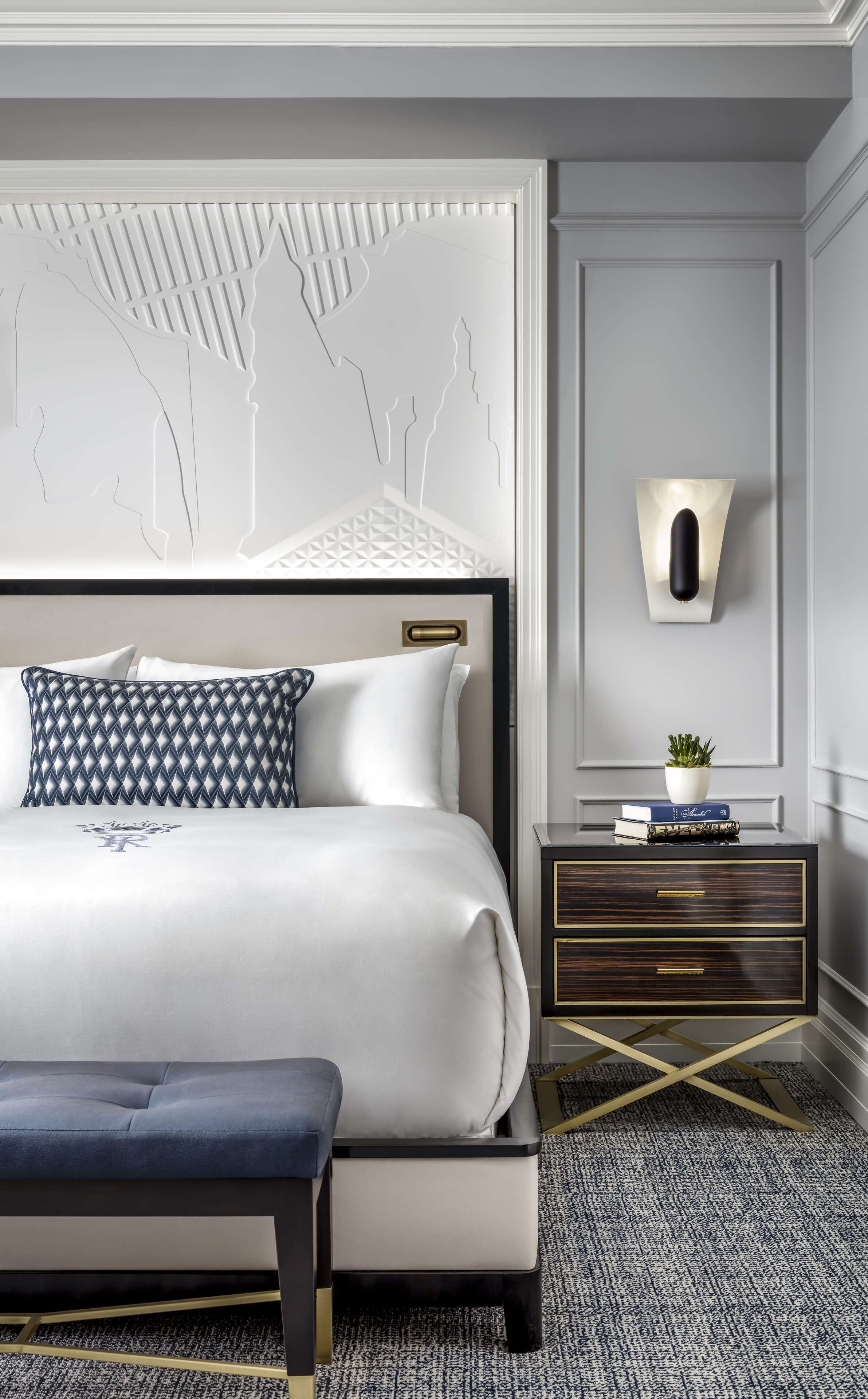 A modern bedroom with a large bed, a bedside table with a lamp, and a decorative wall panel.