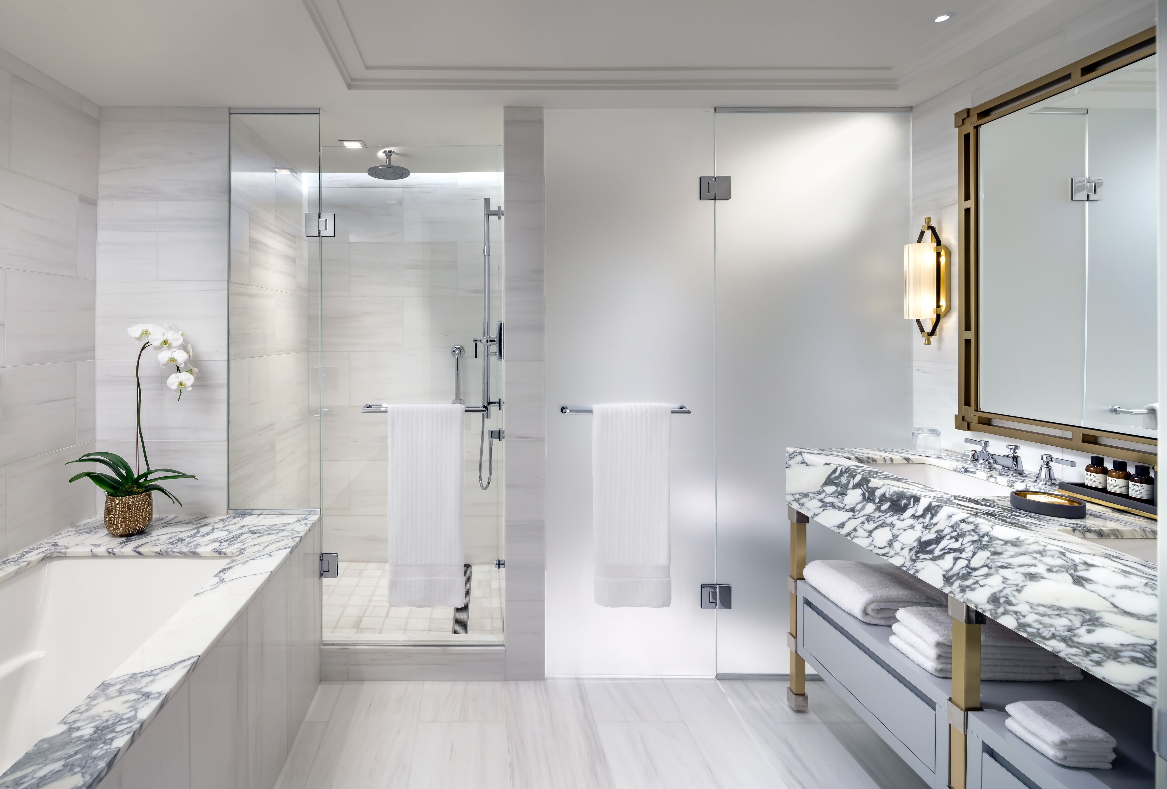A modern bathroom with a marble bathtub, a glass-enclosed shower, and a vanity with a large mirror.