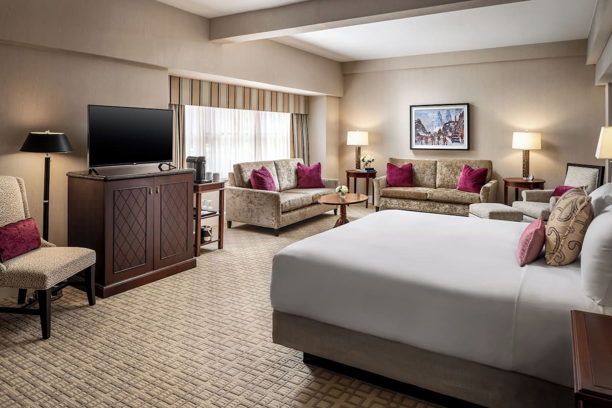 Habitación de hotel con una cama grande, dos sillones, un sofá, un televisor y un cuadro en la pared.