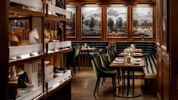 Un restaurante con estanterías de madera, asientos tapizados en verde y vistas a un paisaje a través de amplias ventanas.