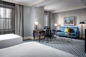 Una habitación de hotel con cama, escritorio, silla, sofá y lámpara.