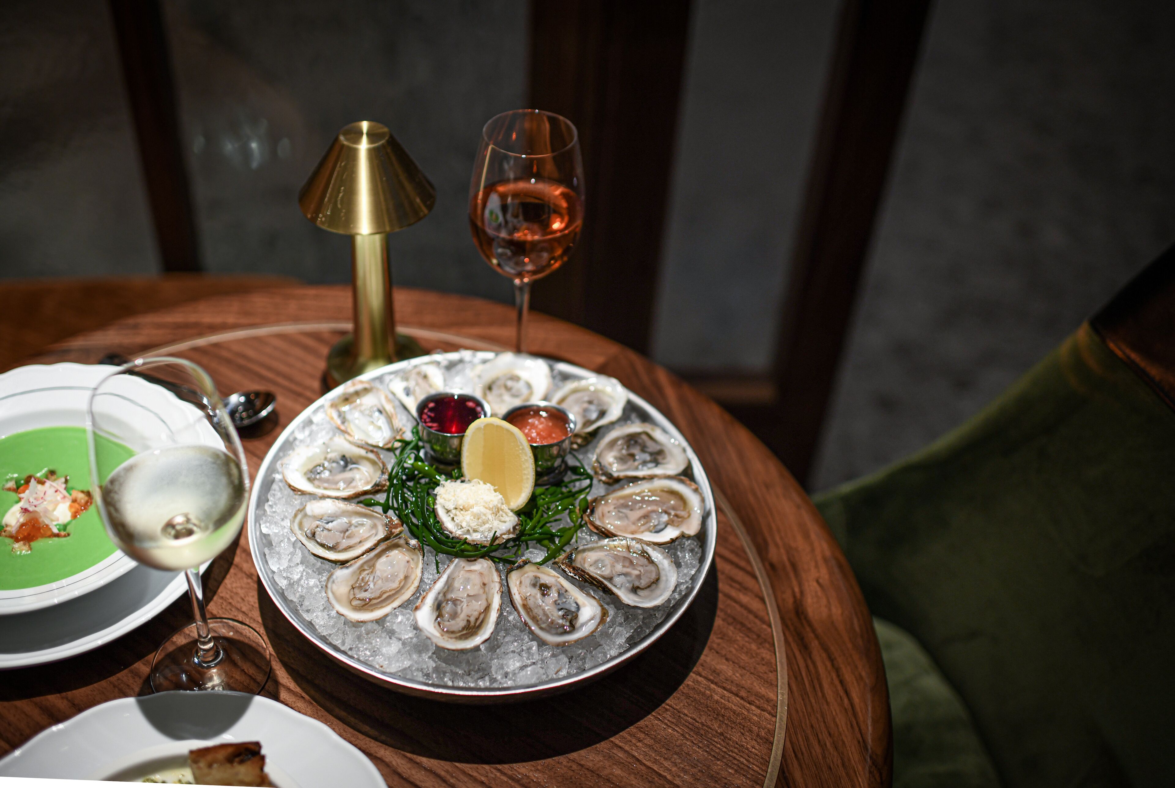 A dining table with a plate of oysters, a glass of wine, and a candle.