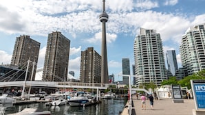 A marina with boats docked, a prominent tower, and modern high-rise buildings in the background.