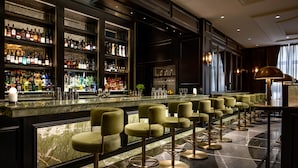 A bar area with a marble countertop, multiple shelves of liquor bottles, and a row of green bar stools.
