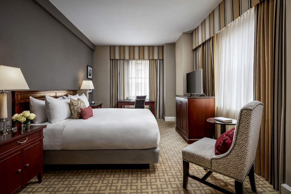 Habitación de hotel con cama, mesitas de noche, escritorio, silla, televisor y cortinas.