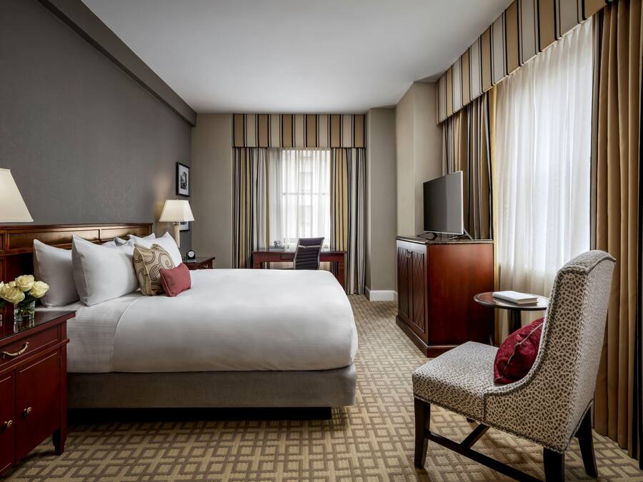A hotel room with a bed, bedside tables, a desk, a chair, a TV, and curtains.