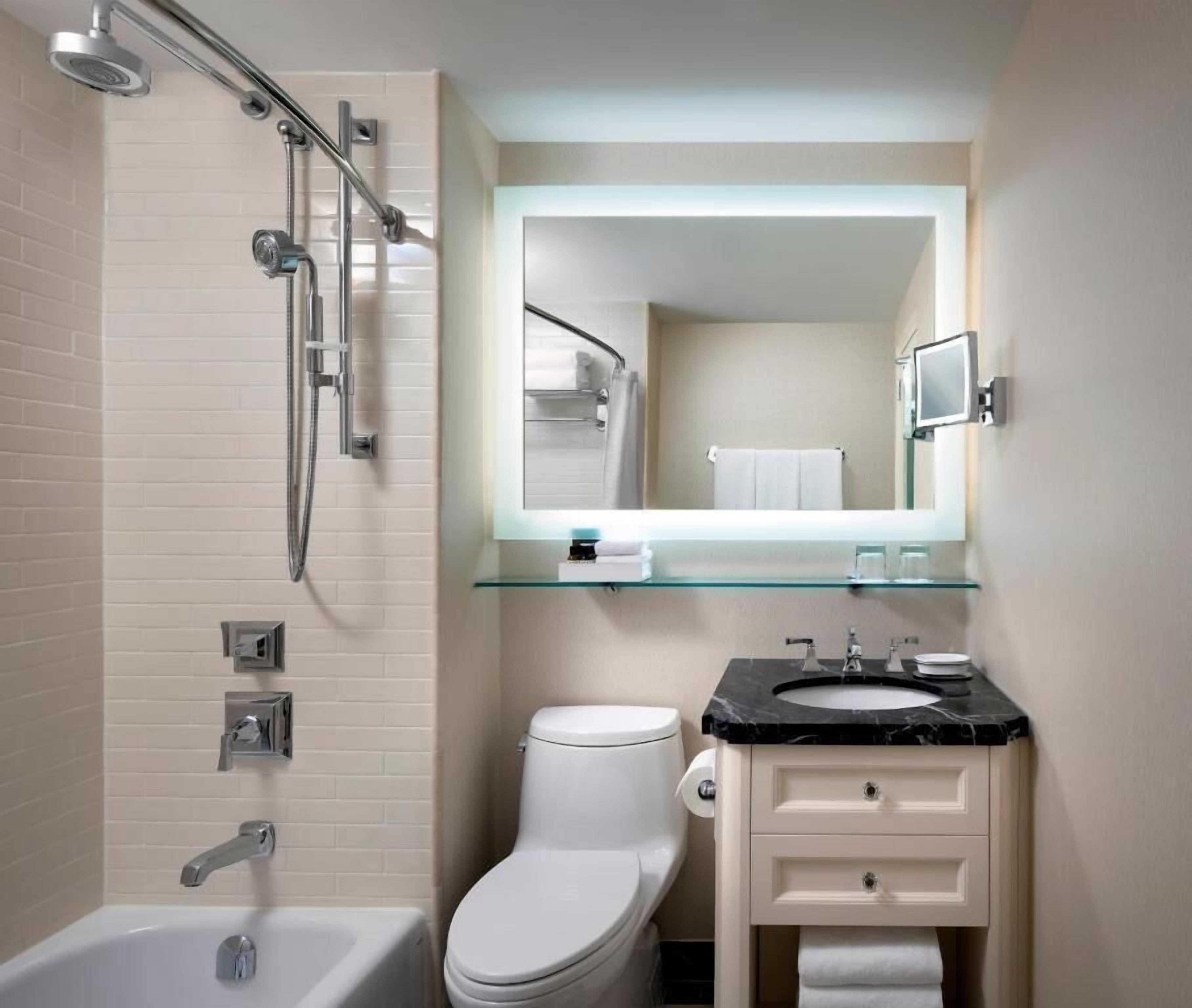 Een moderne badkamer met een douchecabine van glas, een wit toilet, een wastafel met een zwart aanrechtblad en een spiegel boven de wastafel.