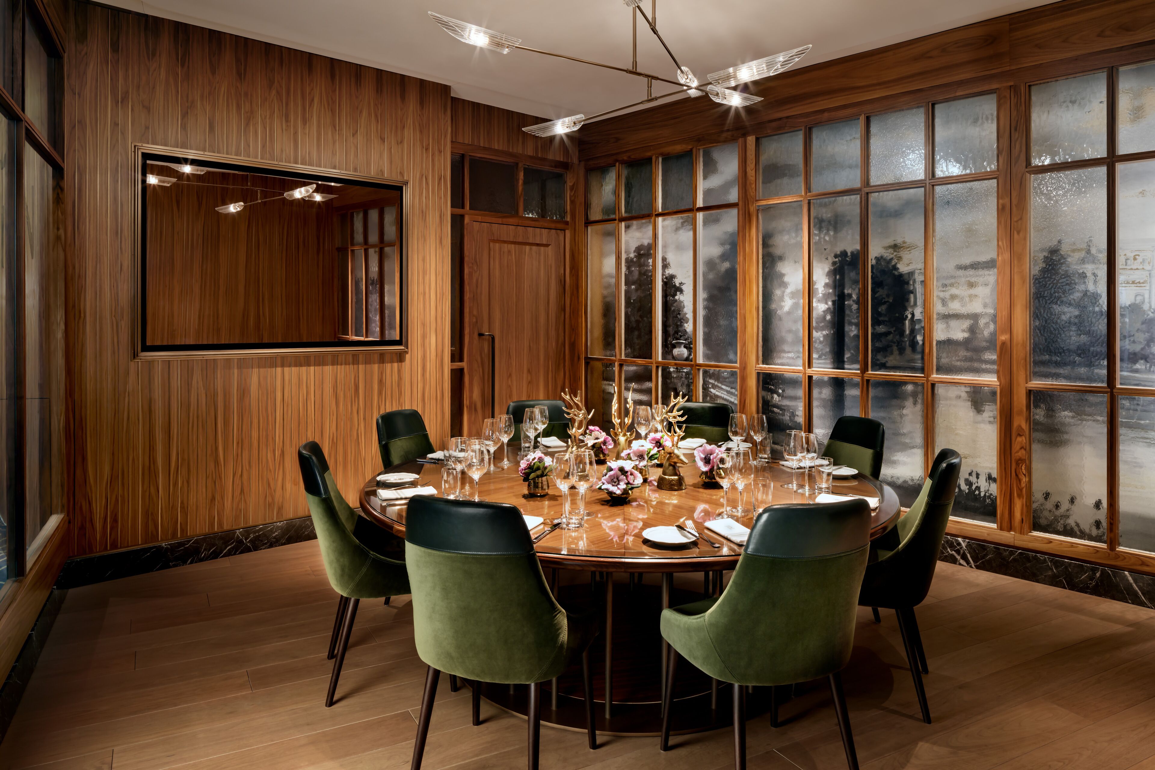 A dining room with a round table set for six, surrounded by green upholstered chairs.