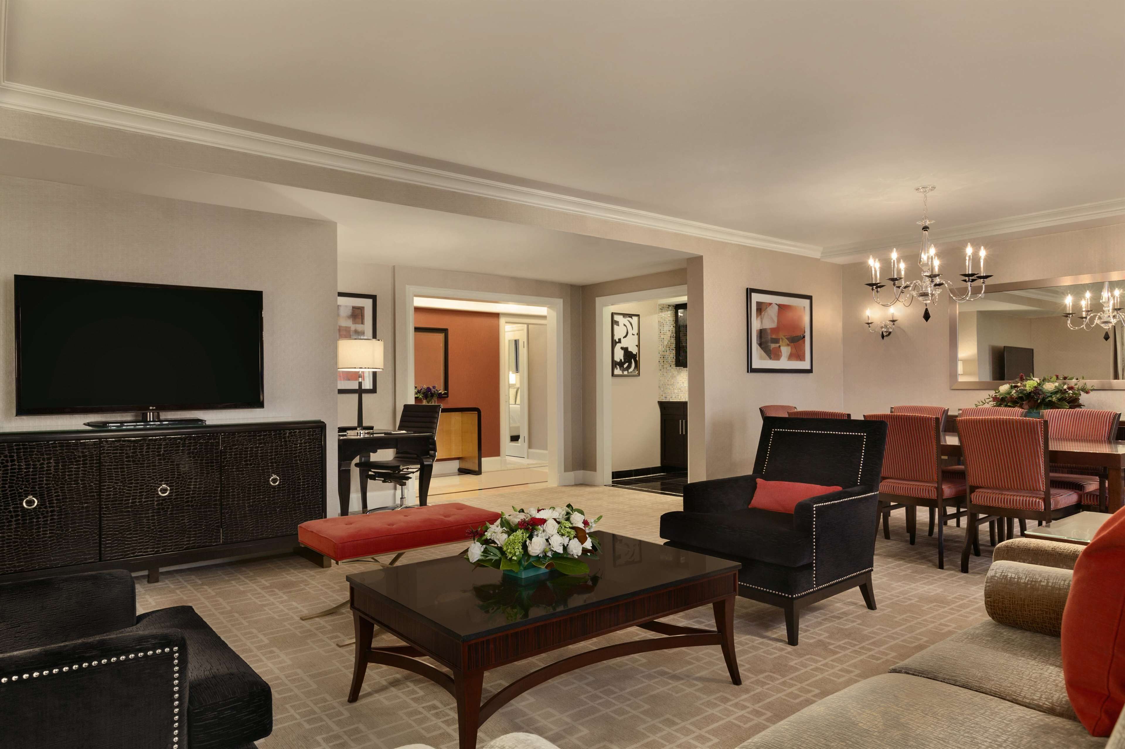 A spacious living room with a flat-screen TV, dark wood furniture, and a red accent chair.