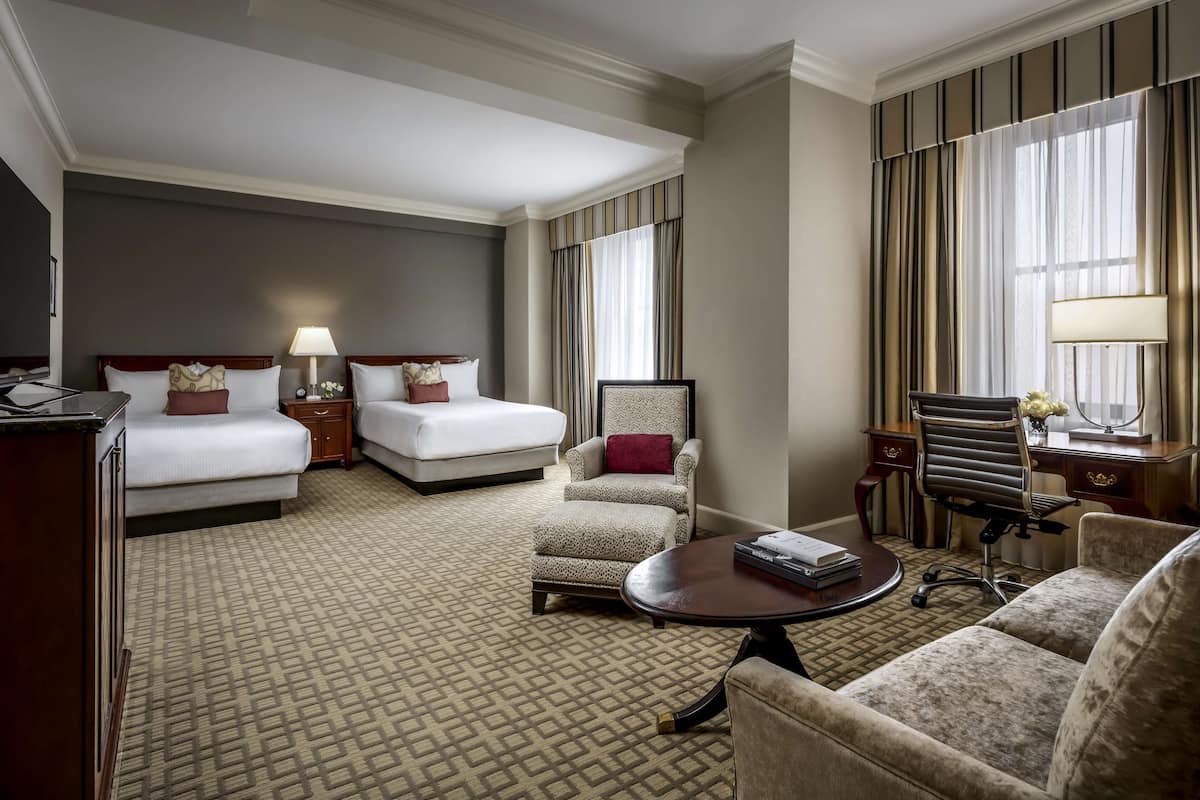 Habitación de hotel con dos camas, un escritorio, una silla, un sofá y una mesita.