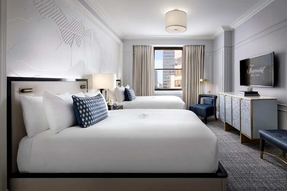 Habitación de hotel con dos camas, televisión, escritorio y vistas a la ciudad.