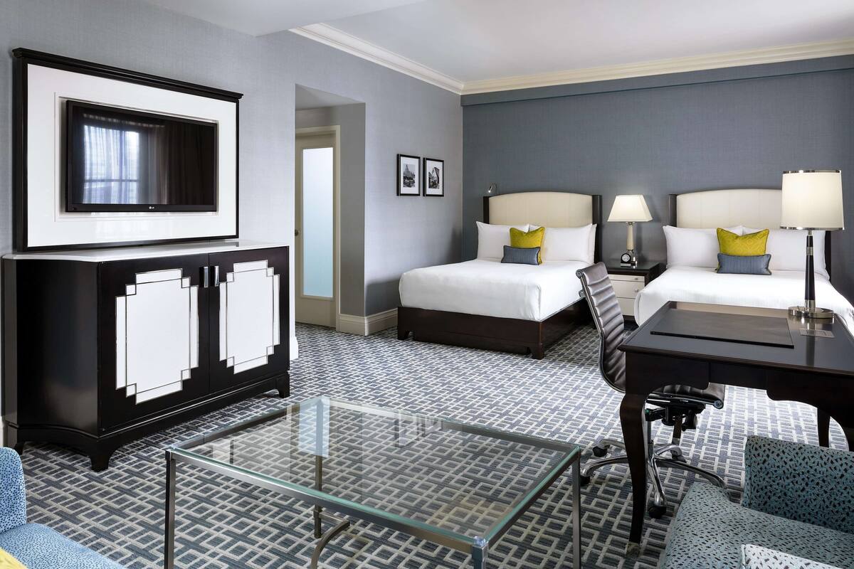 Una habitación de hotel con cama, escritorio, silla, televisor y cómoda.