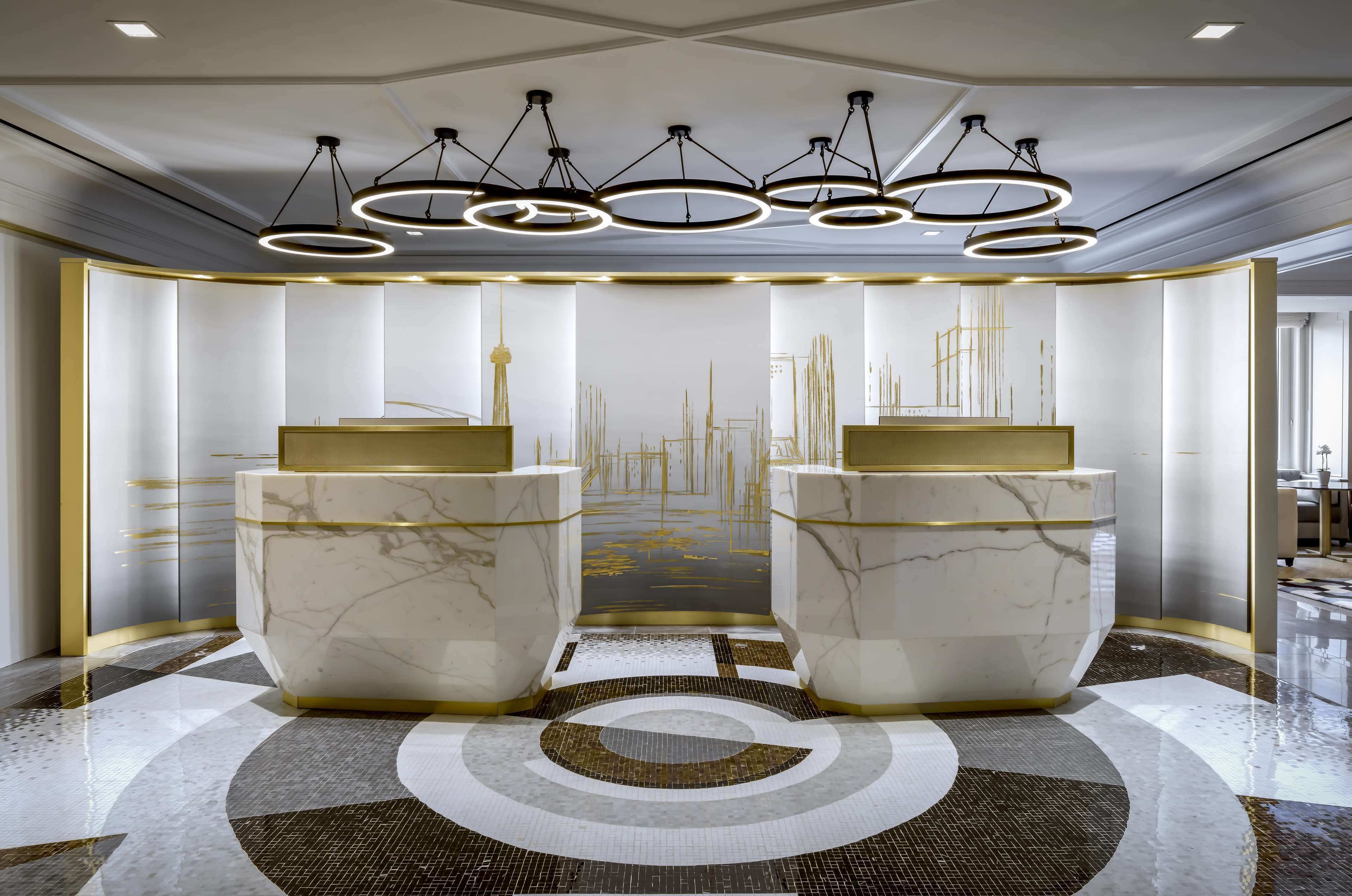 A modern lobby with marble reception desks, a geometric patterned floor, and a ceiling with circular light fixtures.