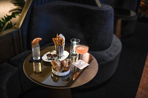 Een ronde tafel met een dienblad waarop een cocktail, een glas water, een klein bordje met frietjes en een bord met twee gebakjes staan.