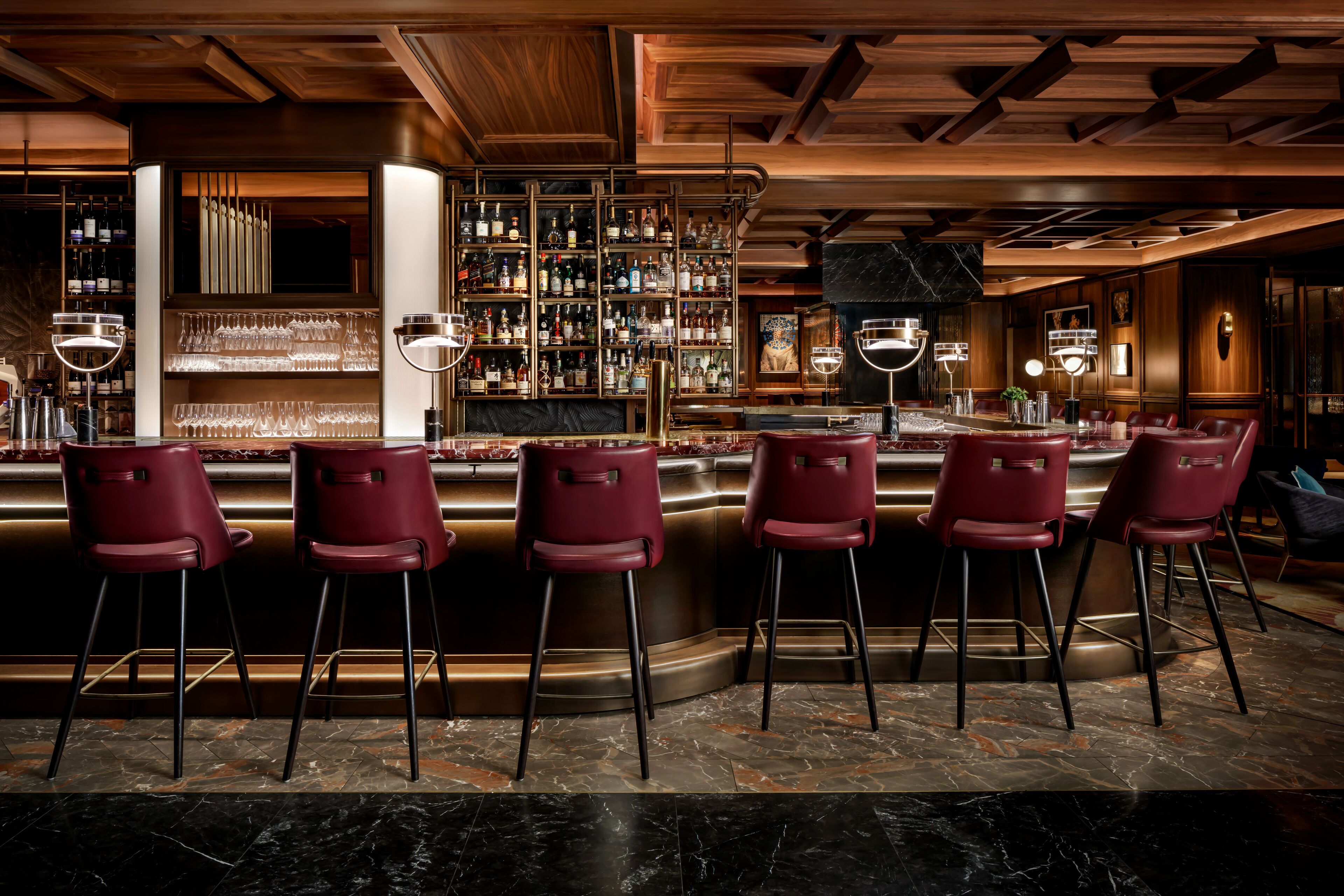 A bar area with a marble floor, red bar stools, and a well-stocked liquor shelf.