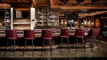 A bar area with a marble floor, red bar stools, and a well-stocked liquor shelf.