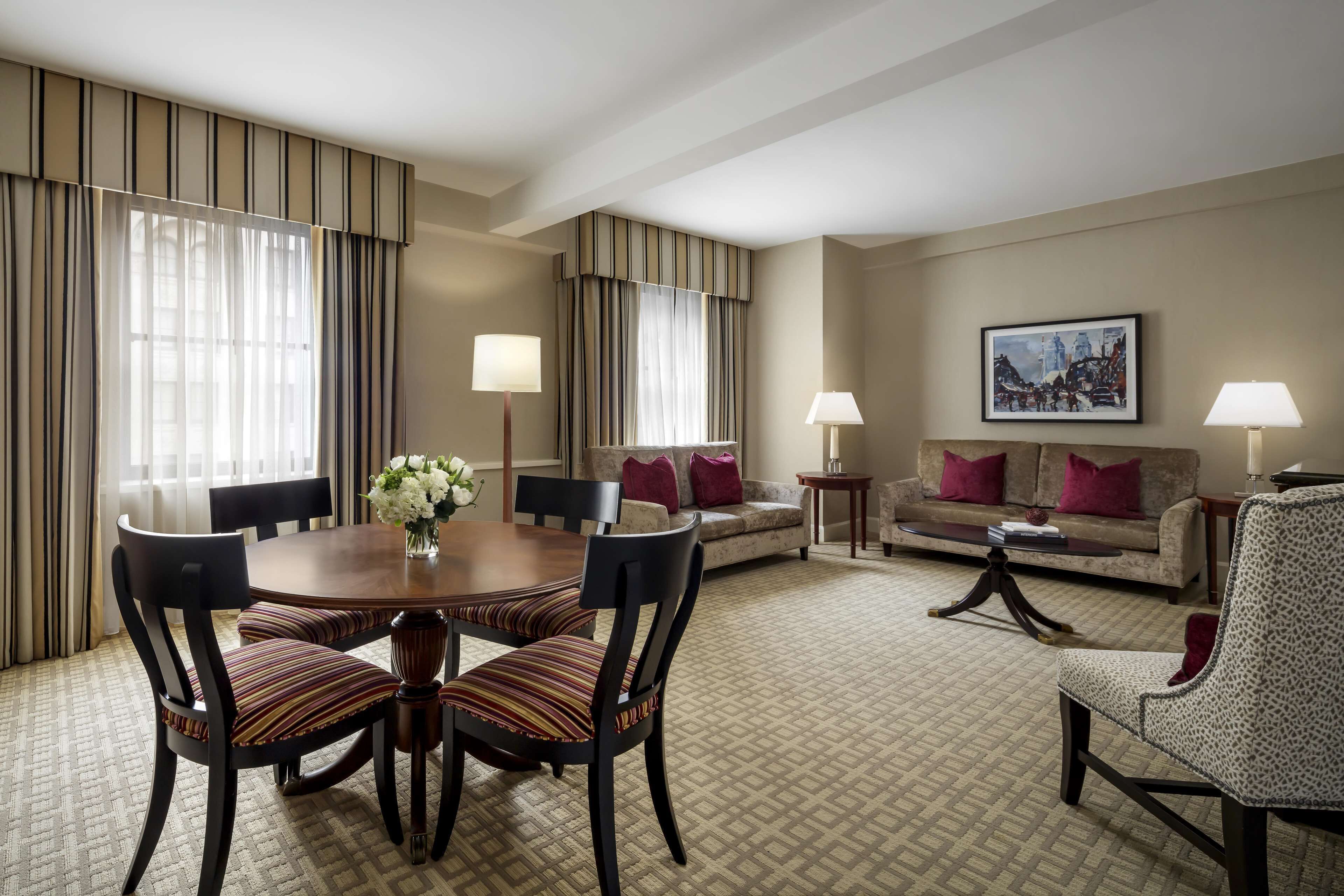 Habitación de hotel con mesa de comedor, sillas, sofá, mesa de centro y un cuadro en la pared.