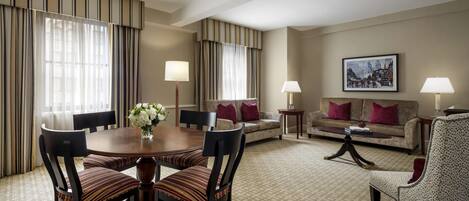 Habitación de hotel con mesa de comedor, sillas, sofá, mesa de centro y un cuadro en la pared.