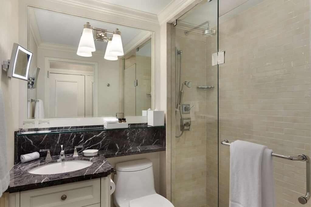 A modern bathroom with a marble sink, white toilet, and a glass-enclosed shower.