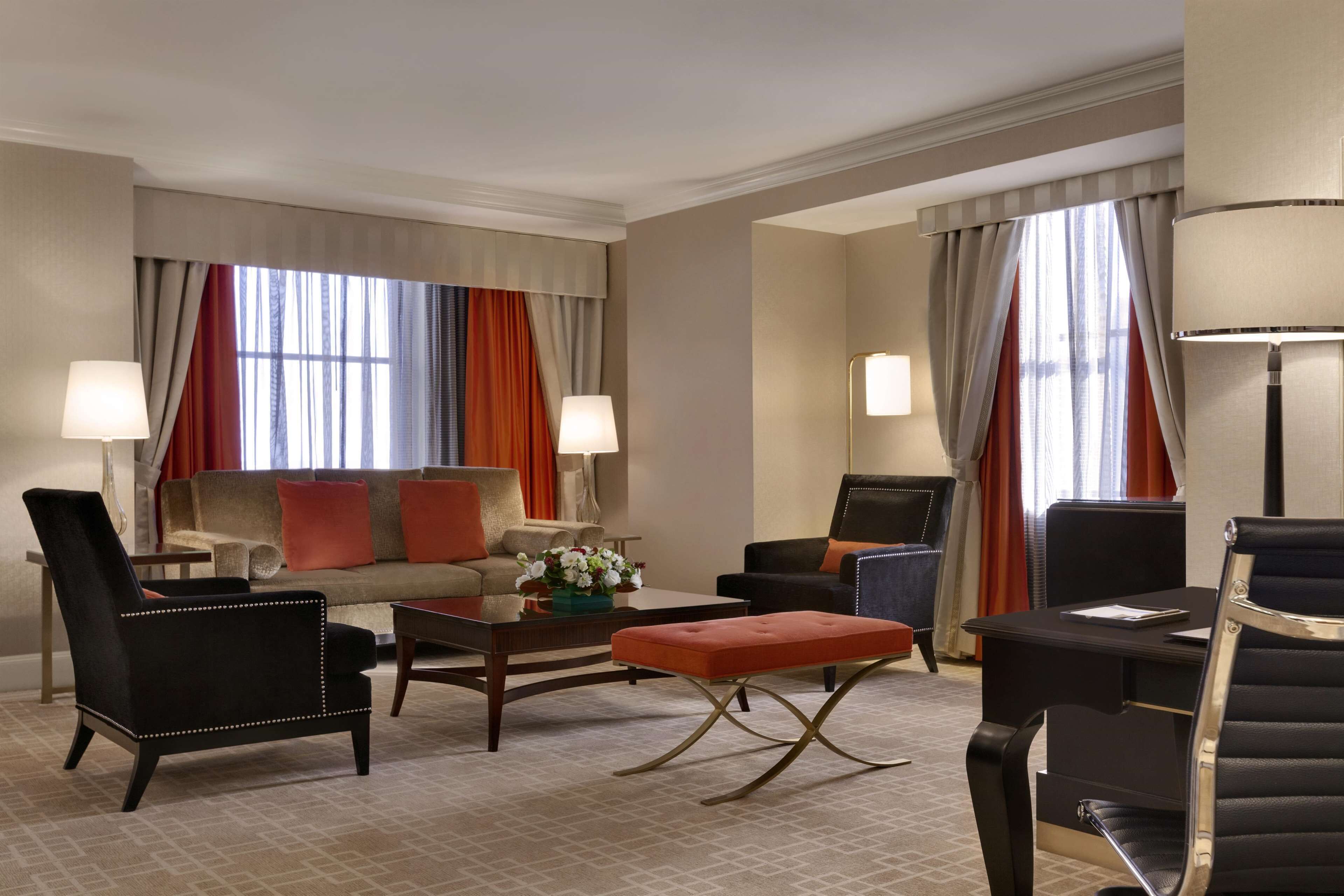 A hotel room with a sofa, armchairs, a coffee table, and a desk with a lamp.