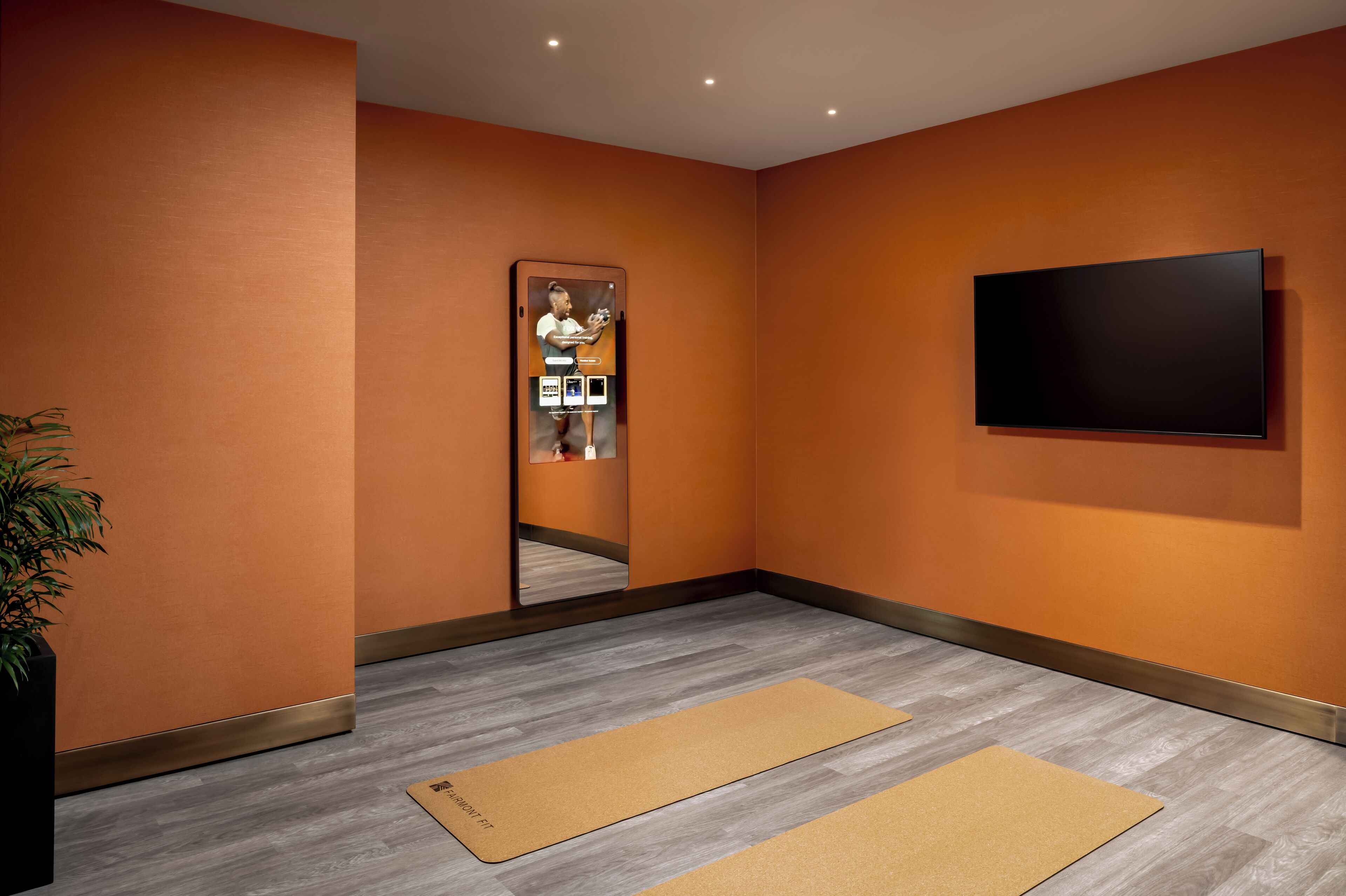 A modern room with orange walls, a large mirror, a flat-screen TV, and two yoga mats on the floor.