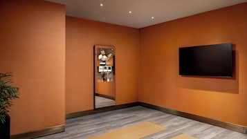 Et moderne værelse med orange vægge, et stort spejl, et fladskærms-tv og to yogamåtter på gulvet.