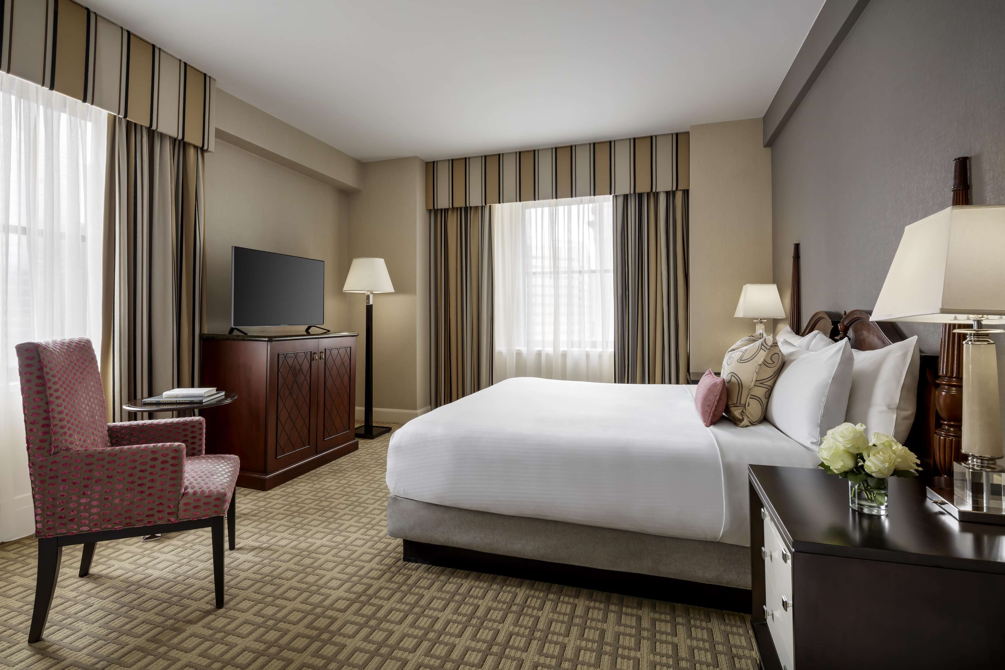 A hotel room with a bed, a TV, a desk, a chair, and a lamp.