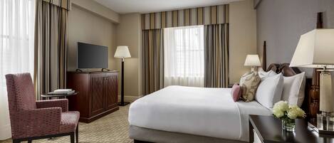 A hotel room with a bed, a TV, a desk, a chair, and a lamp.
