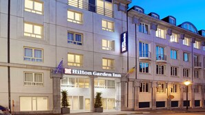 Un hotel de varios pisos con un llamativo letrero de Hilton Garden Inn, ventanas amplias y un diseño arquitectónico clásico.