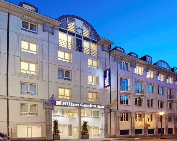 Un hotel de varios pisos con un llamativo letrero de Hilton Garden Inn, ventanas amplias y un diseño arquitectónico clásico.