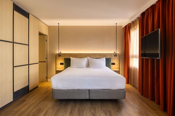 Una habitación de hotel con una cama grande, suelo de madera, televisión y armario.