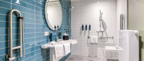 A modern bathroom with a blue tiled wall, a large mirror, a shower area, and a sink with a towel rack.