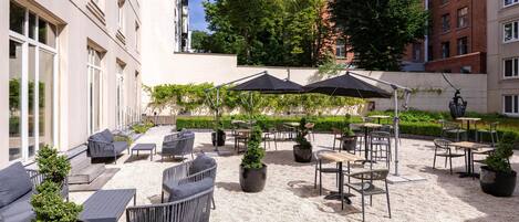An outdoor seating area with tables and chairs, surrounded by potted plants and umbrellas.
