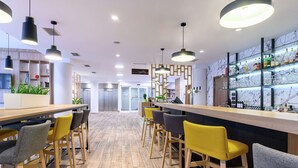 Zona de bar moderna con taburetes de madera, iluminación colgante y una estantería bien surtida con botellas y vasos.