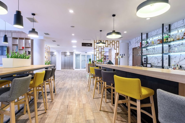 A modern bar area with wooden bar stools, pendant lighting, and a well-stocked shelf with bottles and glasses.