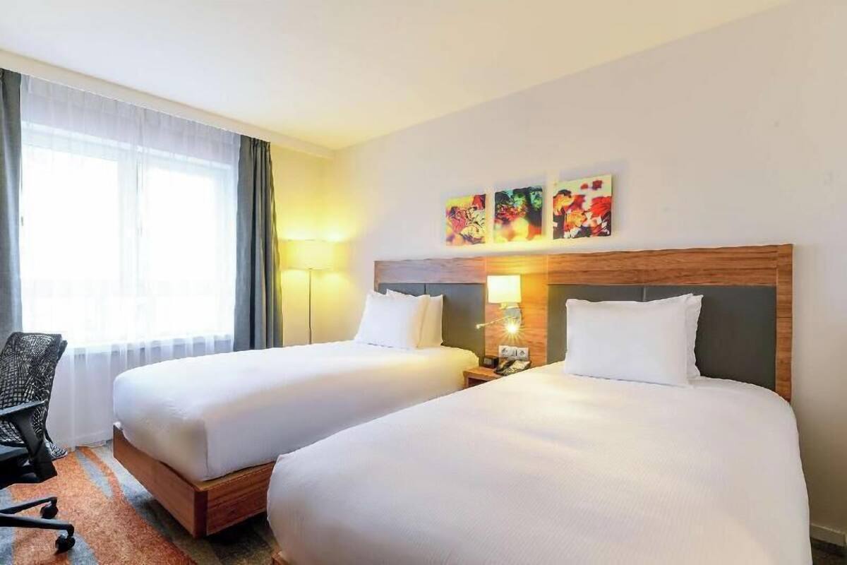 A hotel room with two beds, a desk, a chair, and artwork on the wall.