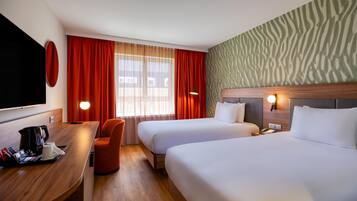 Een hotelkamer met twee bedden, een bureau met koffiezetapparaat, een stoel en een televisie.