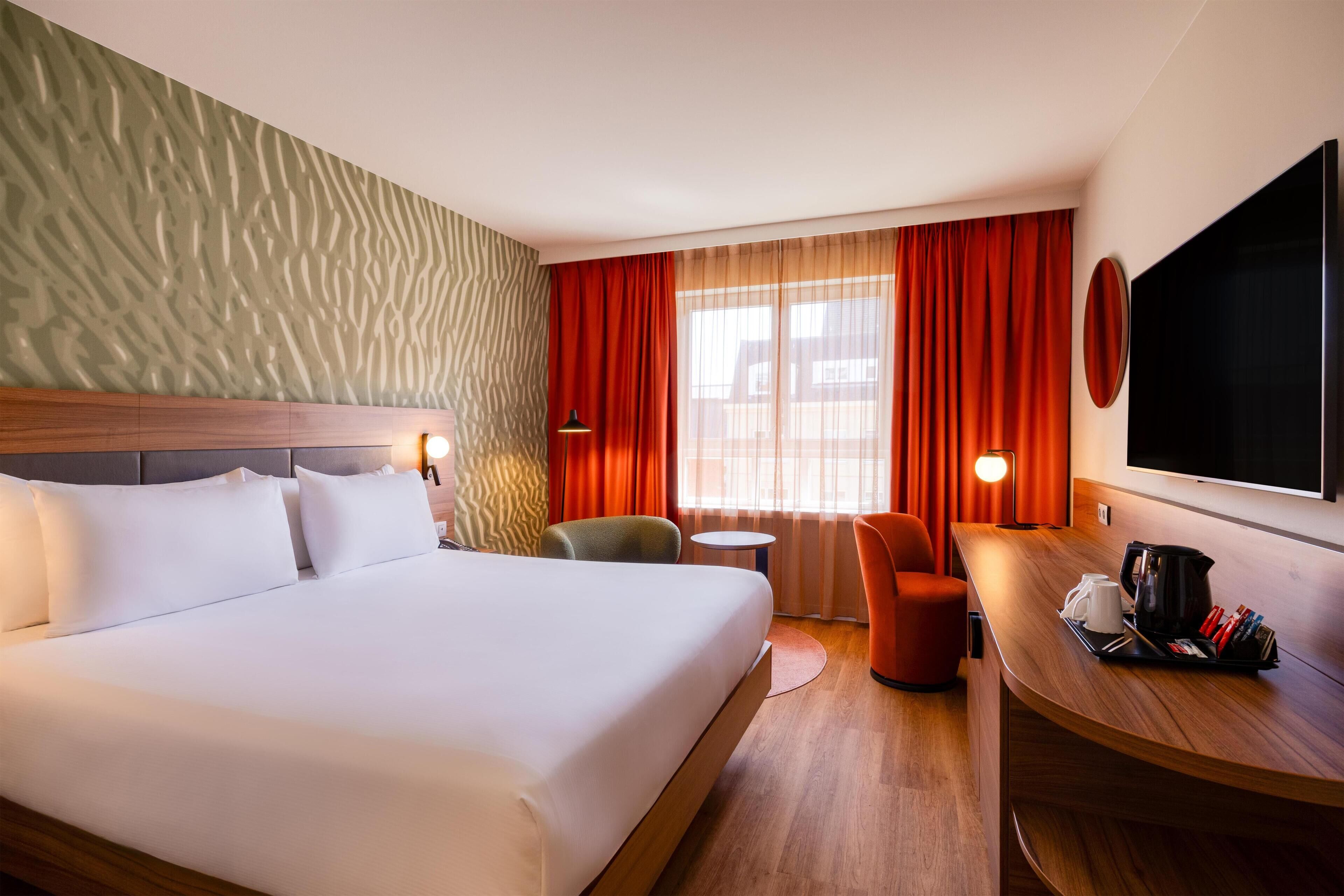 Une chambre d’hôtel avec un grand lit, un bureau avec une machine à café, une chaise et un téléviseur.