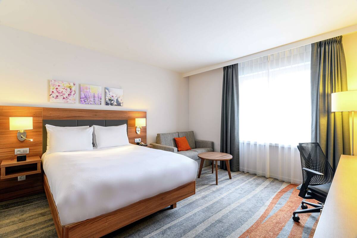 A hotel room with a large bed, a desk, a chair, a sofa, and a small table.