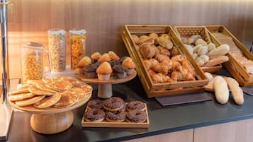 Une variété de produits de boulangerie, notamment des crêpes, des muffins, des croissants et des beignets, présentés sur des présentoirs et des plateaux en bois.