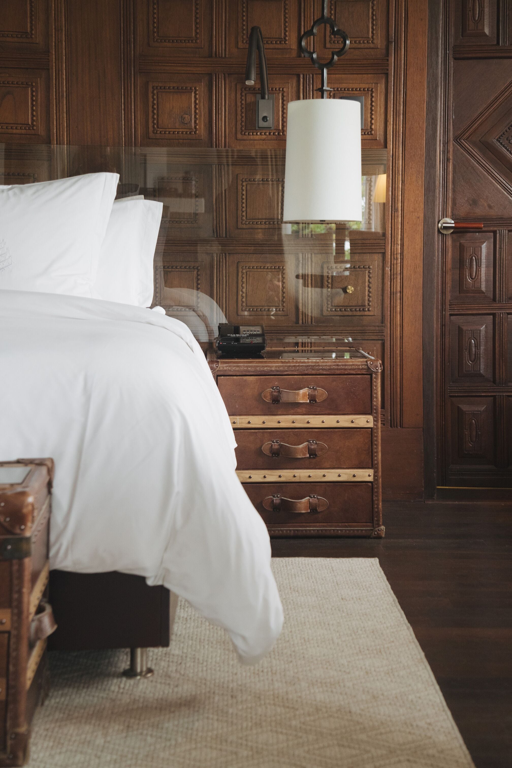 Une chambre à coucher avec une tête de lit en bois, une table de chevet avec une lampe et une valise.