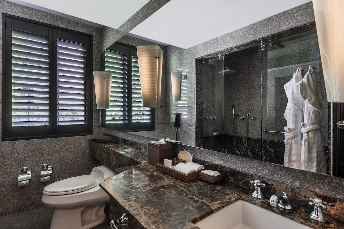 A modern bathroom with a marble countertop, a toilet, a sink, a large mirror, and a shower area.