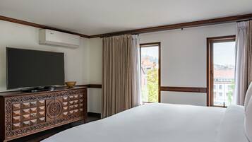 A hotel room with a large bed, a TV on a wooden cabinet, a balcony with curtains, and a city view.