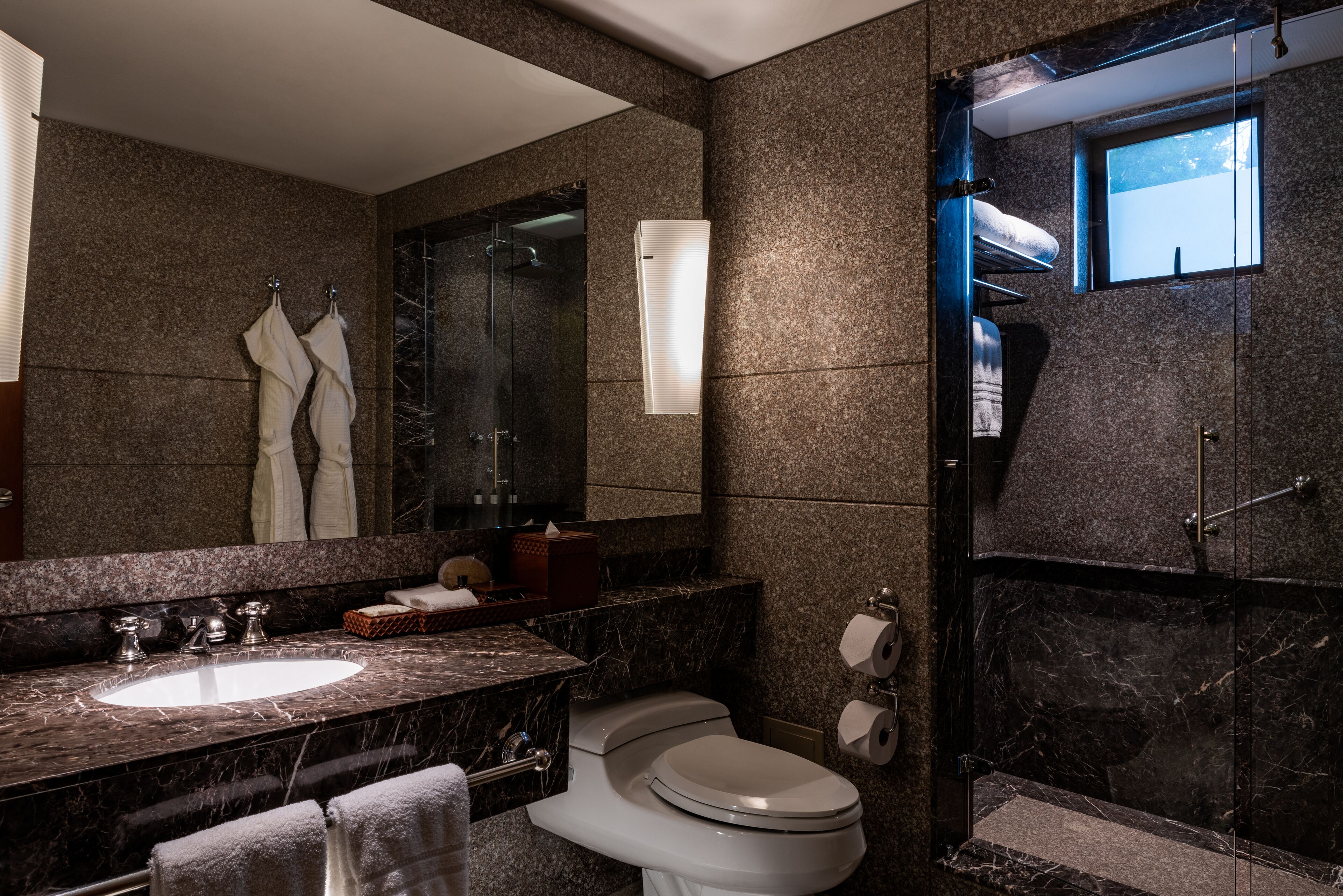 Un baño moderno con lavamanos de mármol, inodoro, cabina de ducha de vidrio y un espejo grande.