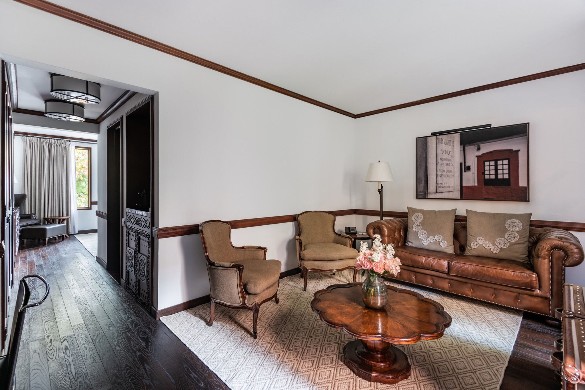 Un salon avec un canapé en cuir marron, deux fauteuils, une table basse en bois et un tapis à motifs.