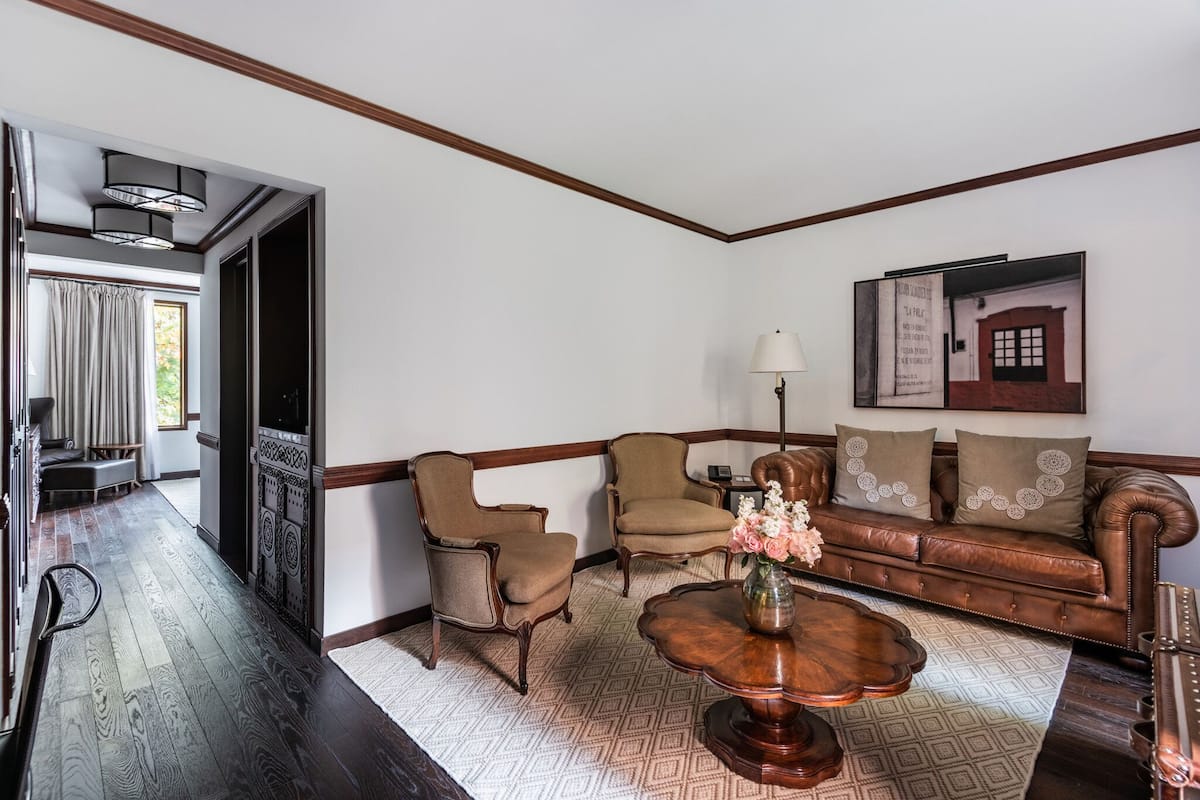 A living room with a brown leather sofa, two armchairs, a wooden coffee table, and a patterned rug.