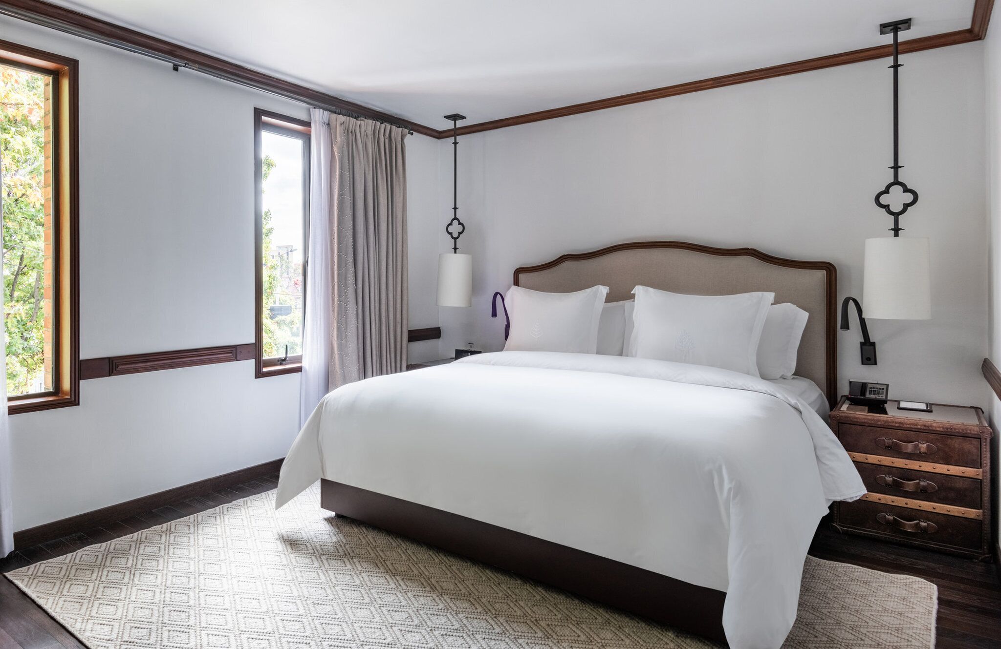 Habitación de hotel con una cama grande, una mesita de noche, una lámpara, una ventana con cortinas y vistas a zonas verdes.