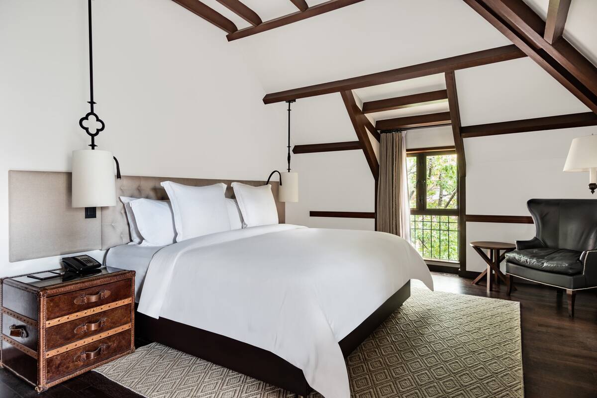 Une chambre avec un grand lit, une table de chevet, une valise, une chaise et une fenêtre donnant sur un paysage verdoyant.